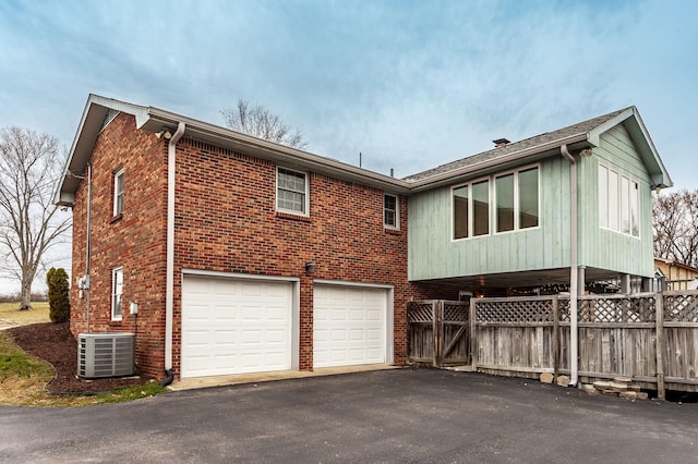 back of property with aphalt driveway, brick siding, fence, and central AC unit