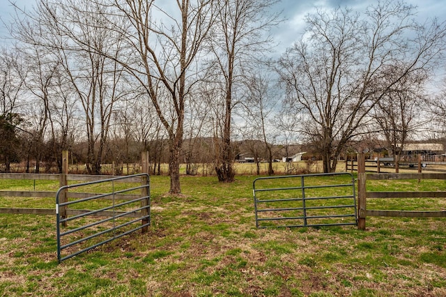 view of gate featuring a rural view, a lawn, and fence