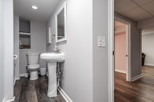 bathroom with a paneled ceiling, toilet, a sink, wood finished floors, and baseboards