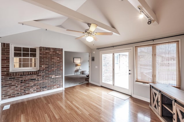 interior space featuring baseboards, brick wall, ceiling fan, wood finished floors, and vaulted ceiling with beams