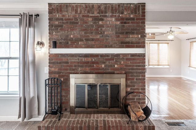 room details featuring visible vents, baseboards, ceiling fan, wood finished floors, and a brick fireplace