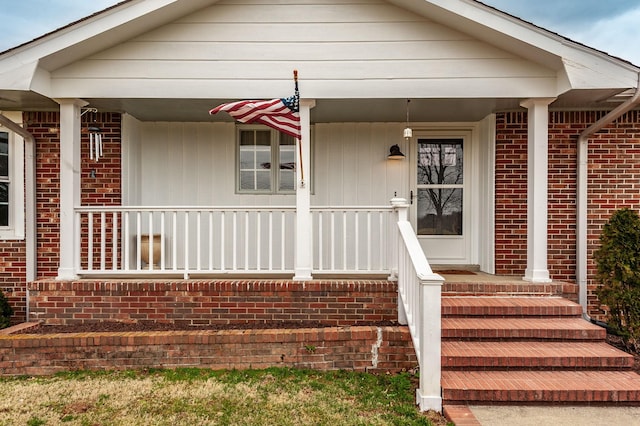 doorway to property featuring a porch and brick siding