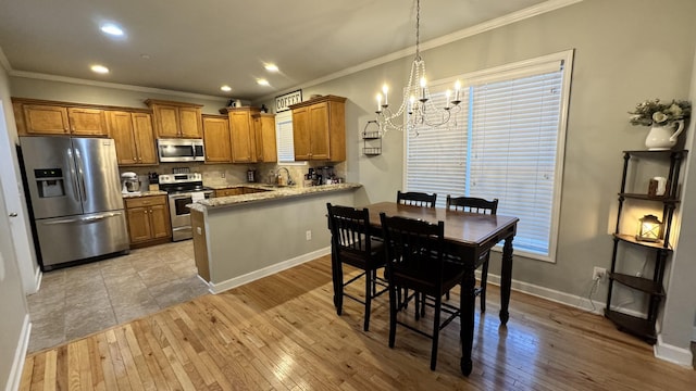 kitchen featuring stainless steel appliances, a peninsula, a sink, light wood finished floors, and brown cabinetry