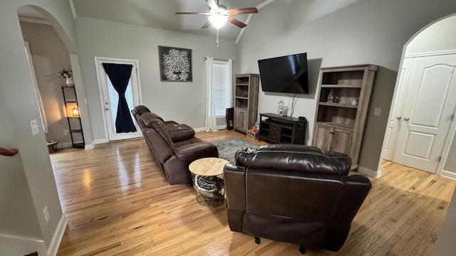 living area featuring arched walkways, baseboards, lofted ceiling, ceiling fan, and light wood-type flooring