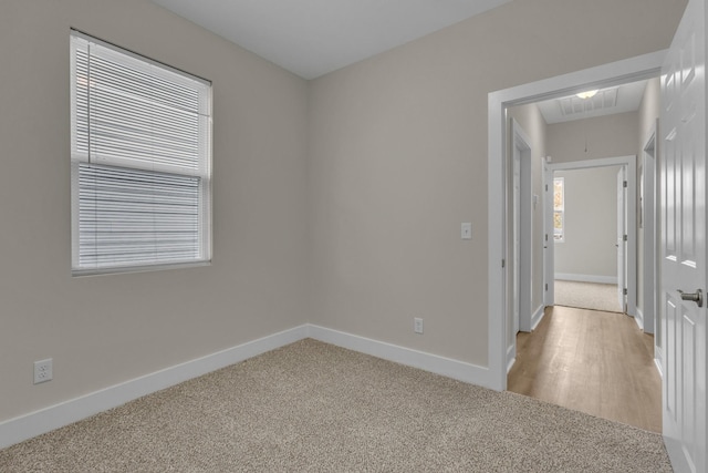 empty room featuring visible vents, light colored carpet, attic access, and baseboards