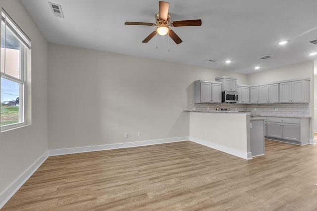 kitchen with light wood-style floors, tasteful backsplash, stainless steel microwave, and baseboards