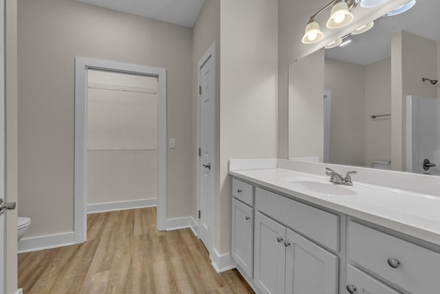 full bath featuring a spacious closet, toilet, vanity, wood finished floors, and baseboards