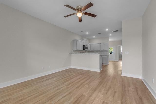 kitchen featuring stainless steel microwave, visible vents, light wood-style flooring, decorative backsplash, and baseboards