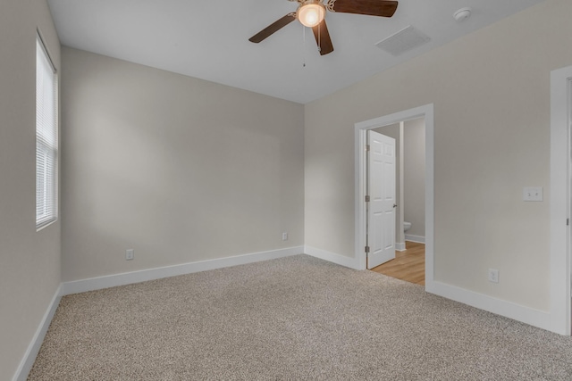 empty room with a ceiling fan, light colored carpet, visible vents, and baseboards