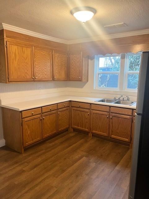 kitchen with dark wood-type flooring, a sink, light countertops, freestanding refrigerator, and brown cabinets