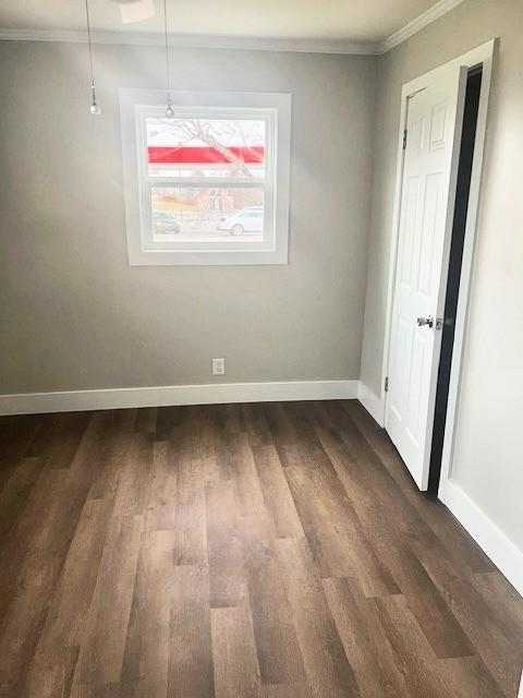 unfurnished room with crown molding, baseboards, and dark wood-style flooring