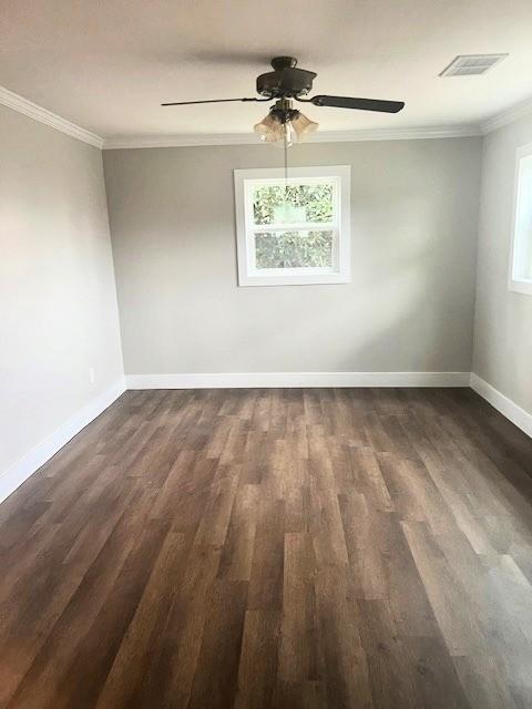 empty room featuring baseboards, visible vents, a ceiling fan, dark wood-type flooring, and crown molding