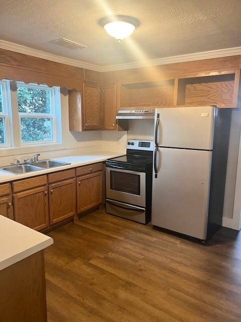 kitchen featuring dark wood-style flooring, appliances with stainless steel finishes, brown cabinetry, a sink, and under cabinet range hood