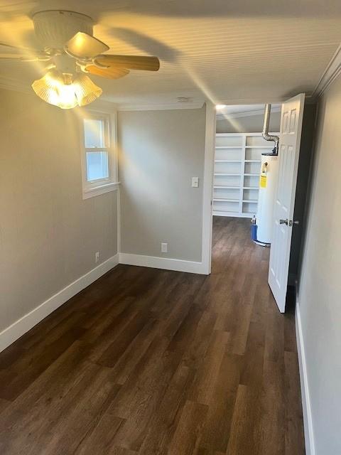 empty room featuring dark wood-style floors, water heater, ceiling fan, and baseboards