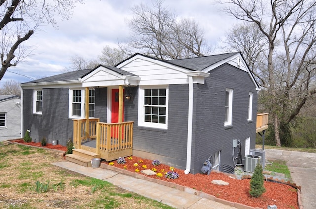 bungalow-style home with an attached garage, driveway, brick siding, and central AC unit