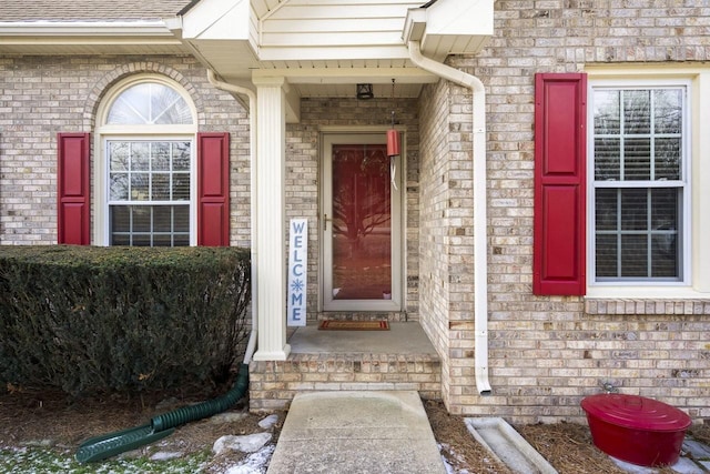 view of exterior entry with brick siding and roof with shingles