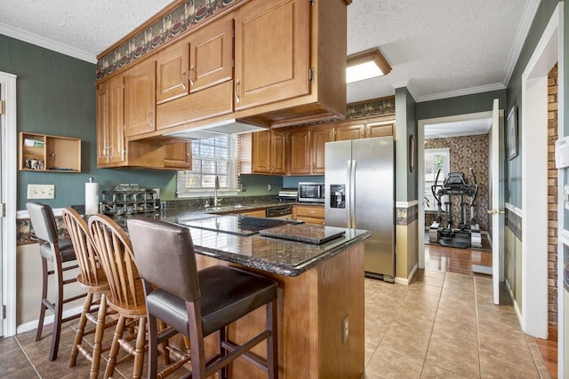 kitchen featuring crown molding, appliances with stainless steel finishes, a sink, dark stone countertops, and a peninsula