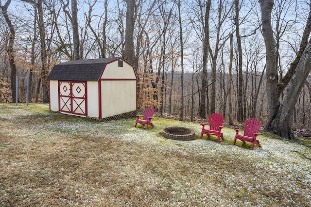 view of yard with a storage shed, an outdoor fire pit, a view of trees, and an outbuilding