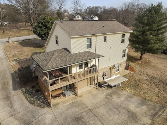 back of property with concrete driveway and roof with shingles