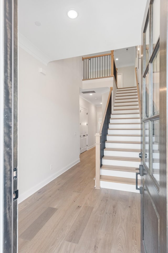 foyer featuring baseboards, wood finished floors, stairs, and crown molding