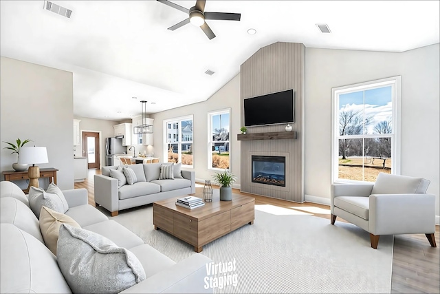 living room with visible vents, light wood-style flooring, a ceiling fan, a large fireplace, and vaulted ceiling