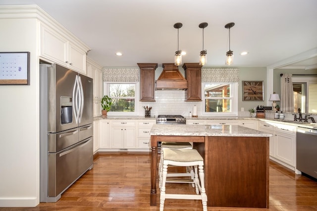 kitchen featuring appliances with stainless steel finishes, a kitchen island, custom exhaust hood, and hardwood / wood-style floors