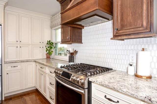 kitchen featuring gas range, premium range hood, light stone counters, and backsplash