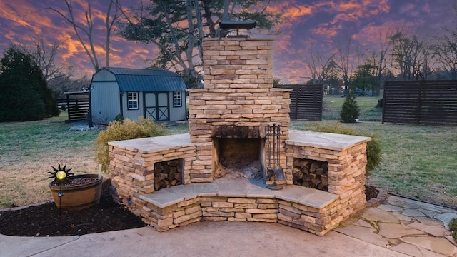 patio terrace at dusk with a storage unit and an outdoor stone fireplace