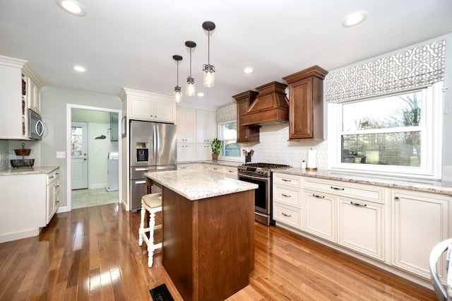 kitchen with appliances with stainless steel finishes, hardwood / wood-style floors, backsplash, and custom exhaust hood