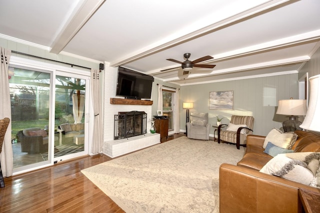 living room with a brick fireplace, ceiling fan, beamed ceiling, and wood finished floors