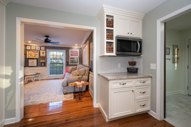 kitchen featuring a wainscoted wall, dark wood-type flooring, white cabinetry, stainless steel microwave, and glass insert cabinets