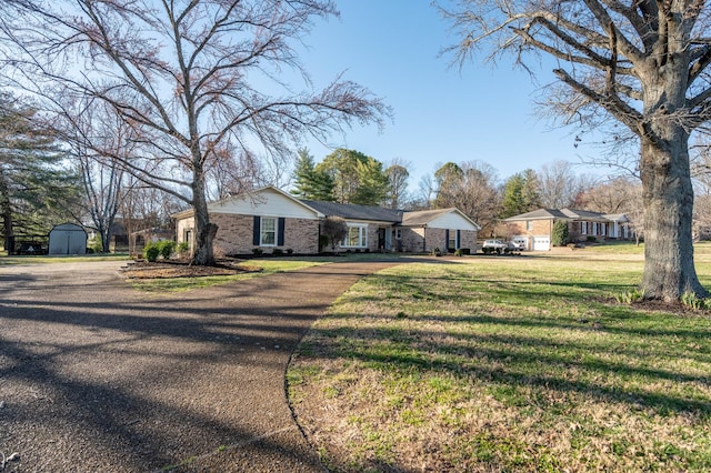 view of front of home featuring an outbuilding, brick siding, a storage shed, driveway, and a front lawn