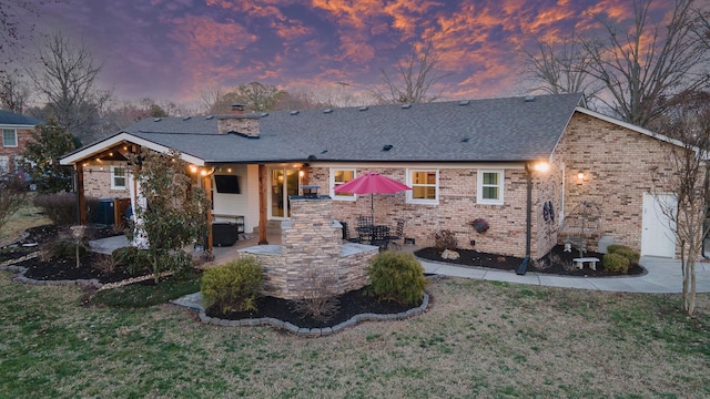 rear view of property featuring brick siding, a yard, a chimney, a shingled roof, and a patio area