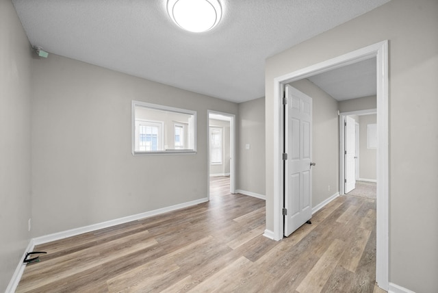 empty room with baseboards, a textured ceiling, and light wood finished floors