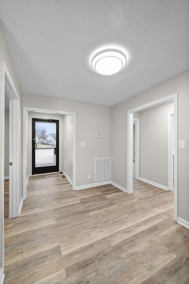 foyer featuring light wood-style flooring, a textured ceiling, visible vents, and baseboards