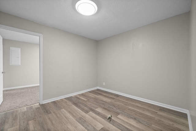 empty room featuring a textured ceiling, baseboards, and wood finished floors