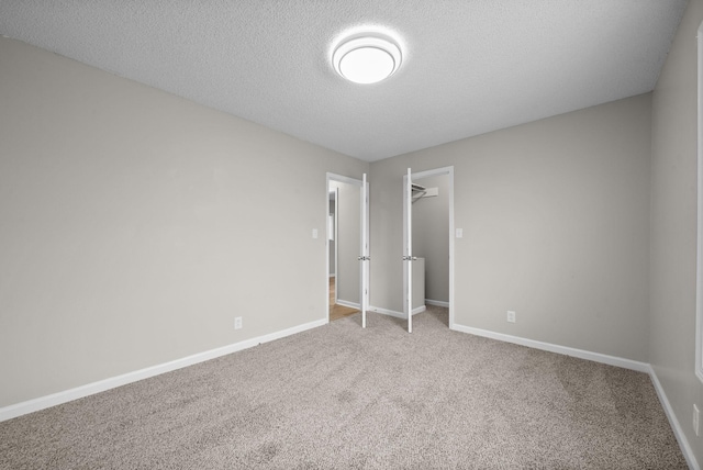 unfurnished bedroom with a textured ceiling, baseboards, a spacious closet, a closet, and carpet