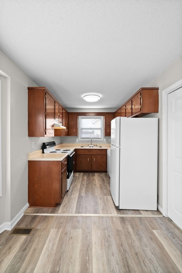 kitchen with under cabinet range hood, range with electric cooktop, light countertops, freestanding refrigerator, and light wood finished floors