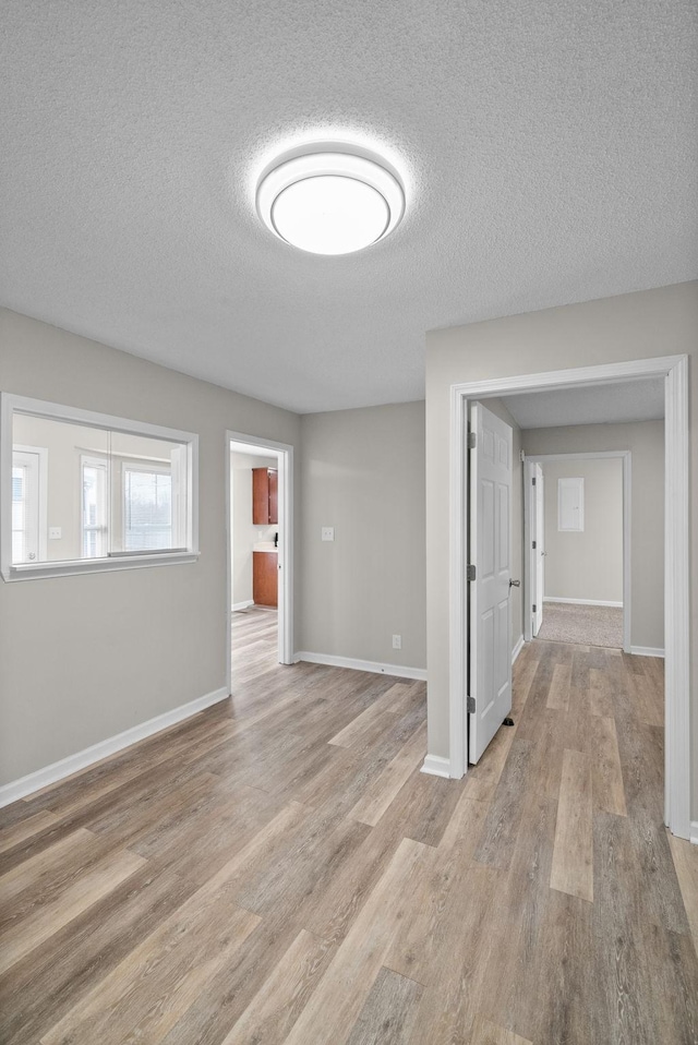 unfurnished room featuring a textured ceiling, light wood finished floors, and baseboards