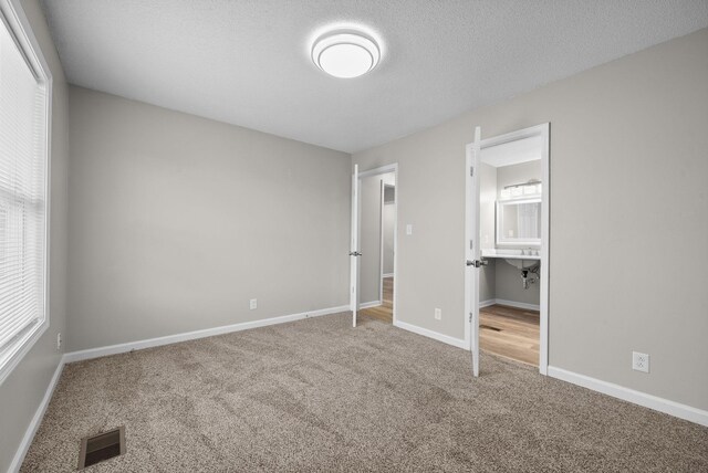 unfurnished bedroom featuring carpet floors, visible vents, connected bathroom, a textured ceiling, and baseboards