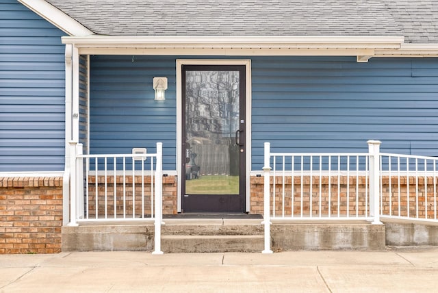 view of exterior entry with a shingled roof and brick siding