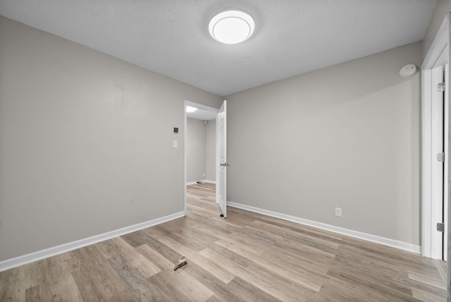 spare room featuring a textured ceiling, light wood-style flooring, and baseboards