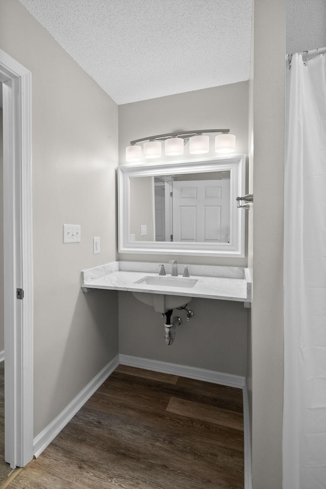 full bathroom featuring a textured ceiling, baseboards, a sink, and wood finished floors