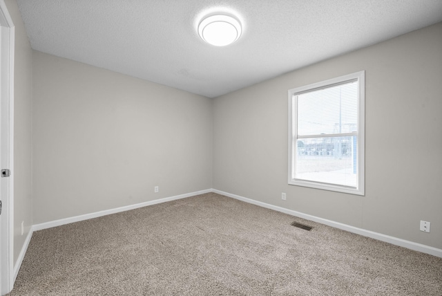 unfurnished room with a textured ceiling, carpet flooring, visible vents, and baseboards