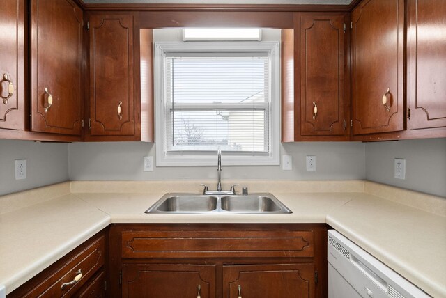 kitchen featuring brown cabinetry, light countertops, white dishwasher, and a sink