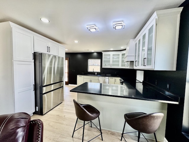 kitchen with dark countertops, appliances with stainless steel finishes, glass insert cabinets, a peninsula, and a sink