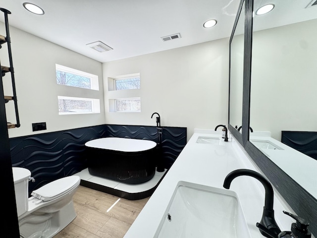 bathroom with double vanity, visible vents, toilet, a sink, and wood finished floors