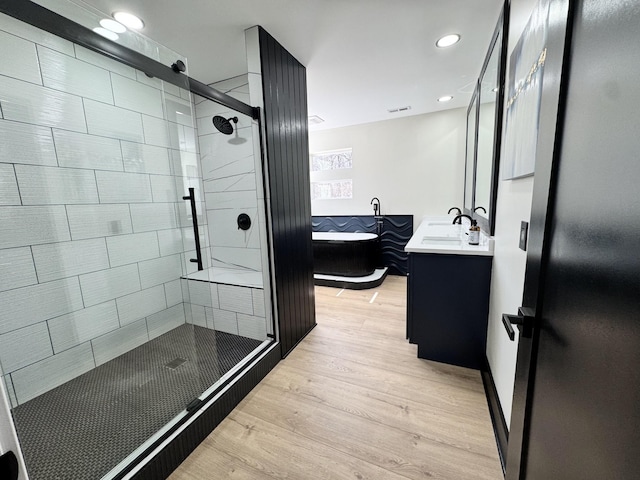 bathroom featuring wood finished floors, visible vents, vanity, a freestanding bath, and a stall shower