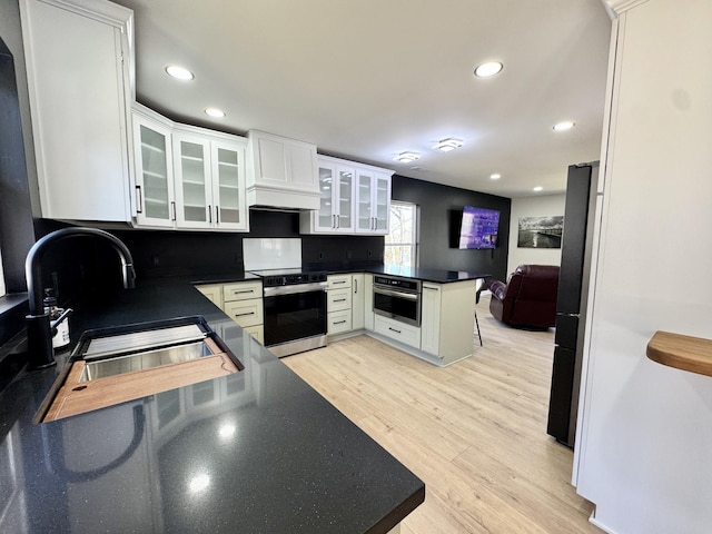 kitchen with range with electric stovetop, light wood finished floors, stainless steel oven, a sink, and a peninsula