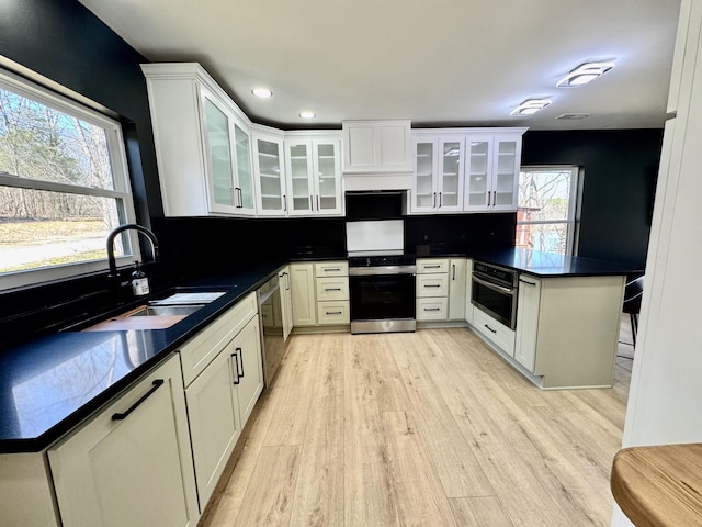 kitchen with decorative backsplash, dark countertops, a peninsula, stainless steel appliances, and a sink